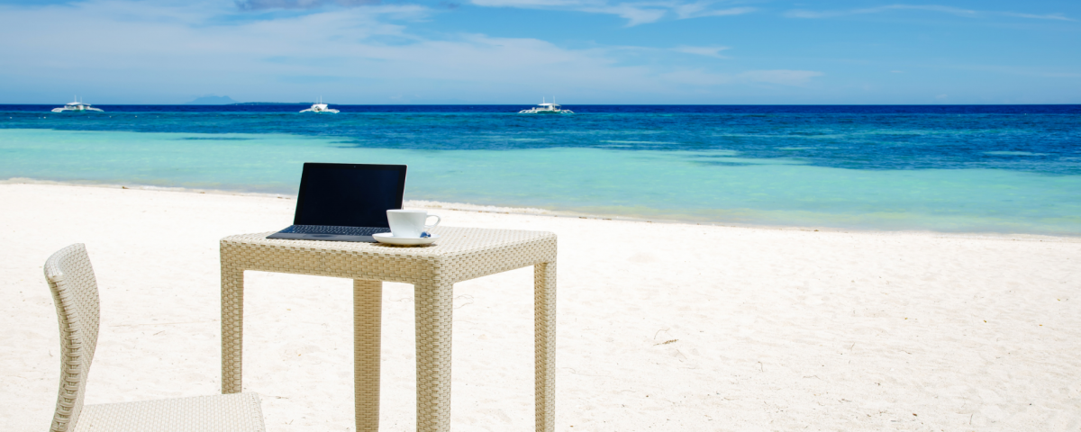 aptop i filiżanka kawy na plaży – symbol powrotu z wakacji do pracy biurowej.