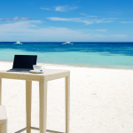 aptop i filiżanka kawy na plaży – symbol powrotu z wakacji do pracy biurowej.